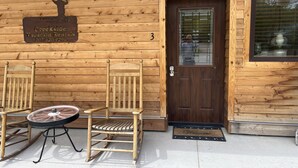Una cabaña de madera con un letrero de Creekside Vacation Rentals, una puerta con ventana y dos mecedoras con una mesita.