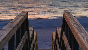 Une jetée en bois menant à une plage, avec un coucher de soleil en arrière-plan.