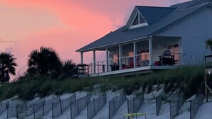 Une maison située en bord de mer, dotée d’un porche couvert et offrant une vue sur la plage.