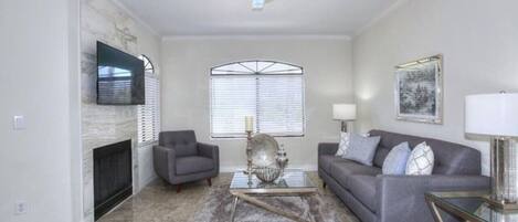 A living room with a fireplace, two sofas, a coffee table, and a ceiling fan.
