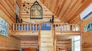 A wooden cabin interior with a loft bedroom, a staircase, and a birdcage on the ceiling. - Luxury Treehouse w/ Grill, Fire Pit, & Pond in Dripping Springs (Dripping Springs)
