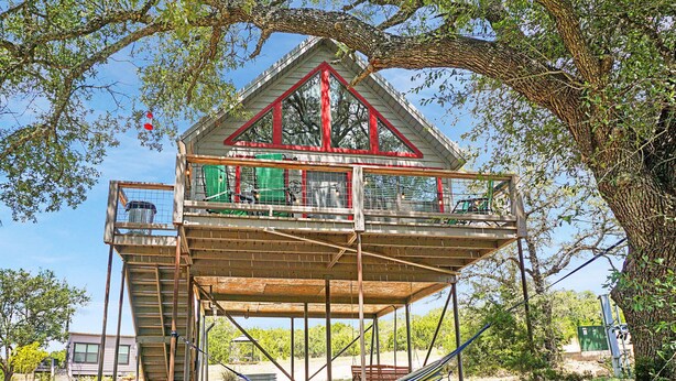 A treehouse with a wooden deck and a red-framed window. - Luxury Treehouse w/ Grill, Fire Pit, & Pond in Dripping Springs (Dripping Springs)