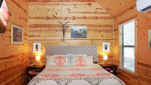Une chambre à coucher aux murs lambrissés, comprenant un lit, deux tables de chevet, une tête de lit et deux lampes fixées au mur.