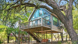 Una casa árbol con terraza de madera, escalera y barandilla metálica.