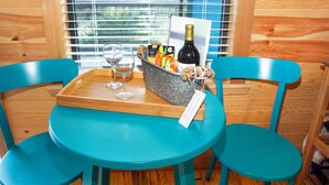 Una mesa azul verdosa con una bandeja, dos sillas, una botella de vino y una cesta con aperitivos y una tarjeta.