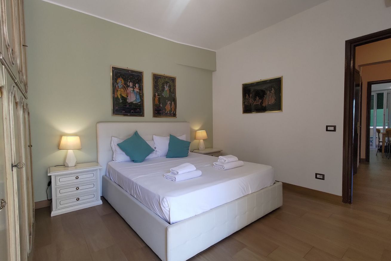 Ein Schlafzimmer mit einem großen Bett, zwei Nachttischen inklusive Lampen, einem kleinen Tischchen und Wandbildern.