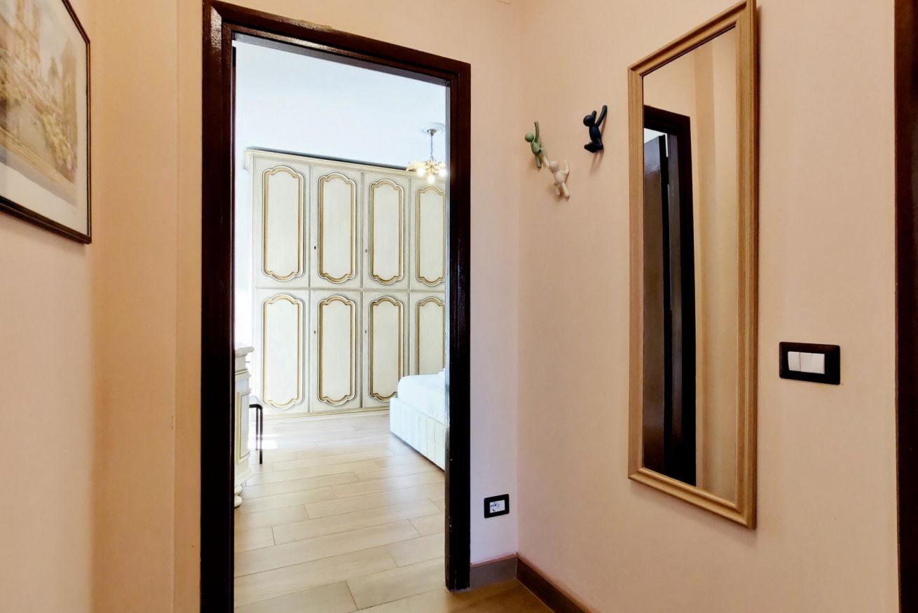 A hallway with a door leading to a room with a large mirror and a light switch on the wall.