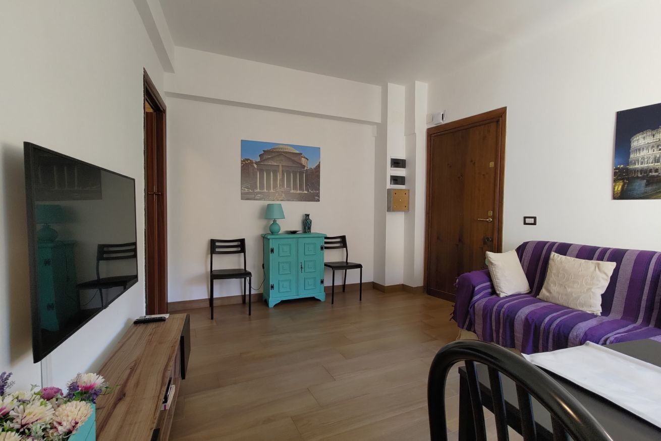 Un salon avec un téléviseur, un canapé, un meuble et un tableau représentant un bâtiment.