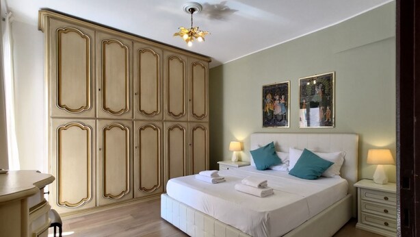 Een slaapkamer met een groot bed, nachtkastjes, een garderobe en een plafondlamp.