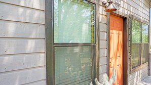 Une maison en bois avec une grande fenêtre, une porte et un porche doté d’un paillasson.