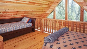 Une chambre confortable dans un chalet, avec un plafond en bois, une grande fenêtre, un lit et un banc recouvert d’une couverture à motifs.