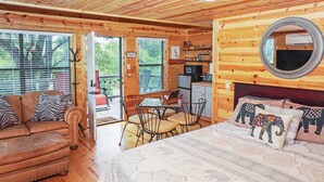 Un chalet confortable avec un intérieur en bois, un lit avec une literie à motifs, un coin repas et une petite cuisine.