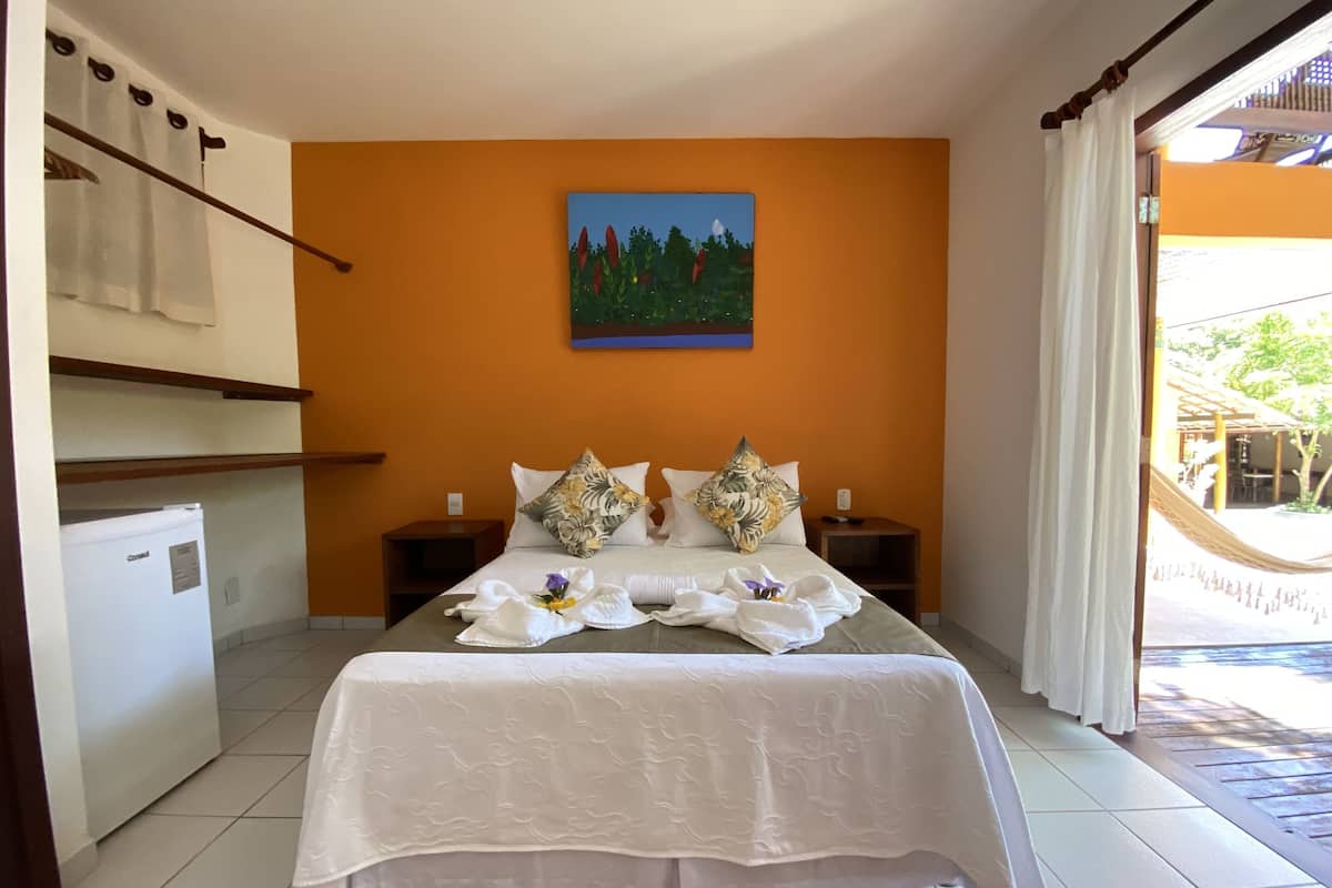 Una habitación de hotel con una cama, un cuadro, un refrigerador y vistas a un espacio exterior.