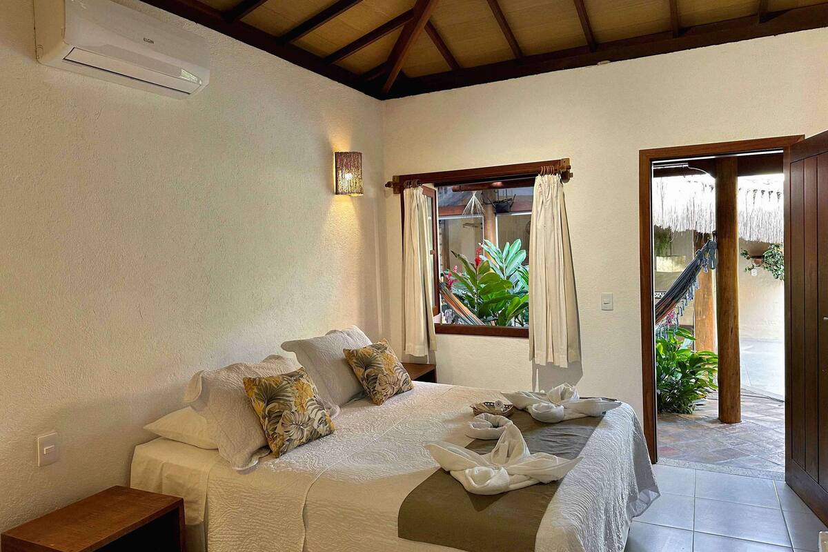 Un dormitorio con cama, almohadas, una mesita de noche, una ventana con cortinas y vistas al exterior.