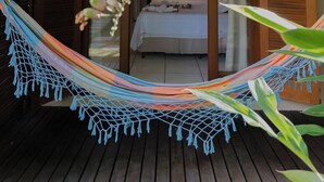 Un hamac suspendu sous une voûte de verdure, donnant sur une pièce avec un lit et une fenêtre.