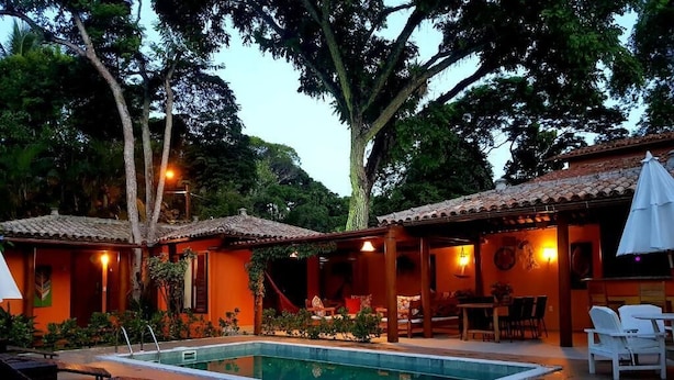 Un espace piscine avec des chaises longues et un coin repas, le tout entouré d’arbres et d’un bâtiment doté d’un toit en tuiles.