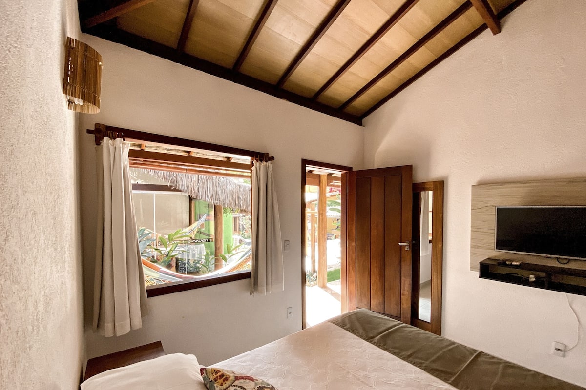 Un dormitorio con cama, televisor montado en la pared y ventana con cortinas.