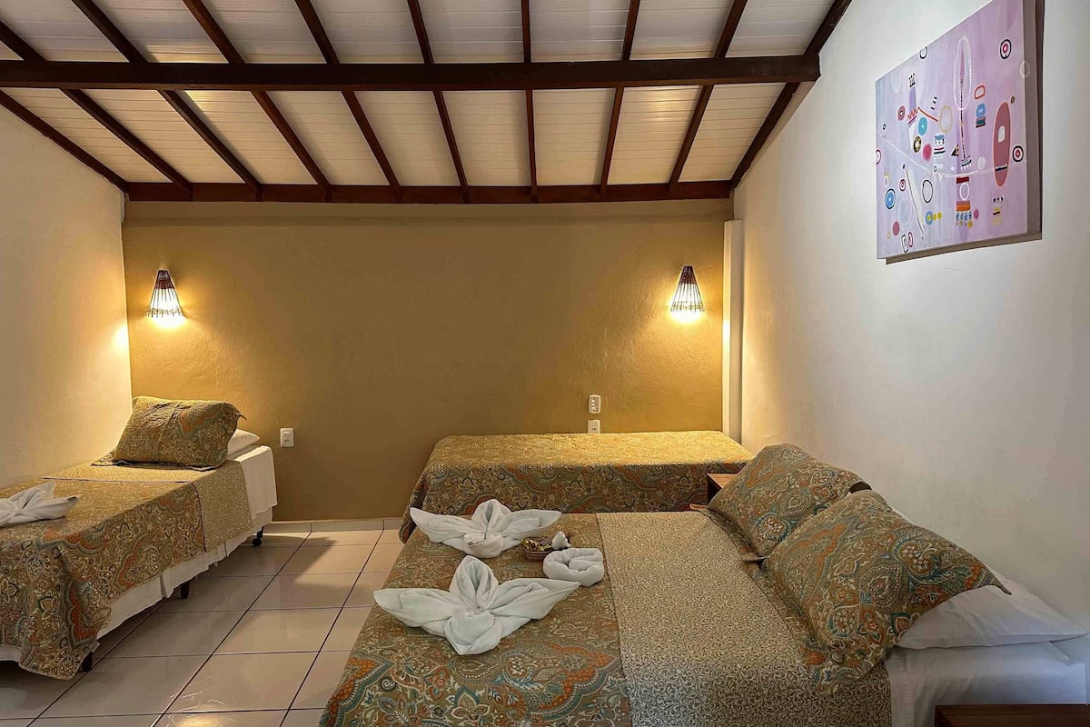 Habitación de hotel con dos camas individuales, una cama grande y un techo con vigas de madera.
