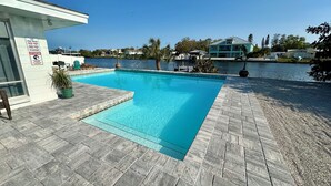 Piscina con agua cristalina azul, rodeada por una terraza empedrada y vista a un lago.