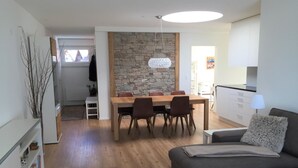 Ett modernt vardagsrum med en soffa, ett matbord med stolar, en köksdel och en vägg av sten.