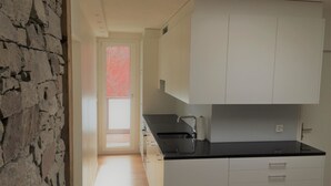 Ett kök med vita skåp, en svart bänkskiva och utsikt över ett rött träd genom ett fönster.
