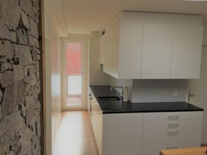 Cucina con mobili bianchi, un piano di lavoro nero e vista su un albero rosso attraverso una finestra.