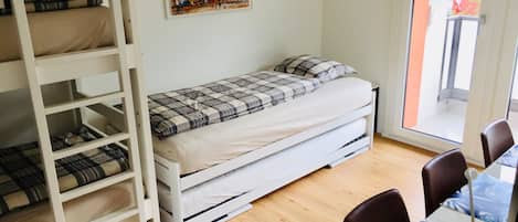 Ein Schlafsaalzimmer mit Etagenbett, einem Einzelbett, einem Tisch mit Stühlen und einem Fenster mit Ausblick.
