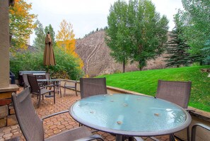 Relax outdoors with a round table and four chairs, surrounded by a grassy lawn and a barbecue grill.