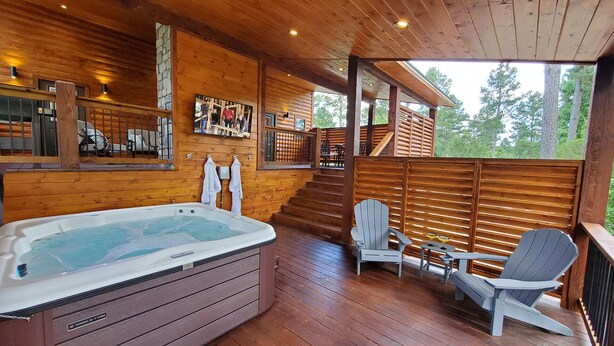 Una terraza de madera con un jacuzzi, una zona de estar cubierta con sillas Adirondack y un muro de piedra con cuadros.