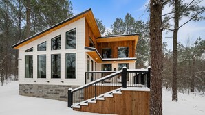 A modern two-story cabin with large windows, a wooden deck, and a staircase leading to the entrance. - Luxury Honeymoon/Small Family, Hot Tub, Firewood Included (Broken Bow)