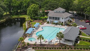 A large swimming pool with lounge chairs and umbrellas, surrounded by a fence and palm trees. - 1st Floor, 2 BR, 2 Bath Sunset Beach 5 minutes to ocean @ Sea Trail Golf Resort! (Sunset Beach)