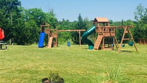 A playground with two wooden play structures, including slides and swings, set in a grassy area with trees in the background. - Beautiful Upgraded Luxury Condo in Great Location with Mtn Views & Great Beds (Pigeon Forge)
