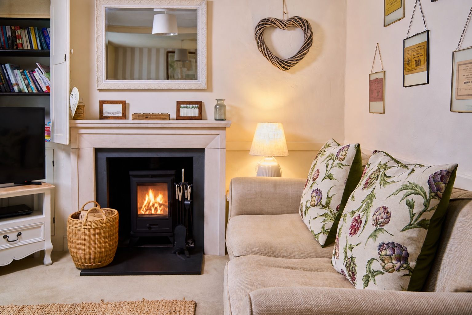 A cozy living room with a fireplace, a sofa with floral cushions, a television, and a bookshelf.