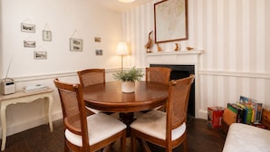 Un comedor con una mesa redonda de madera, cuatro sillas de madera, una lámpara, una chimenea y una estantería llena de libros.