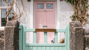 Une porte rose avec une pancarte au-dessus indiquant : « Maggie Puddle Cottage ».