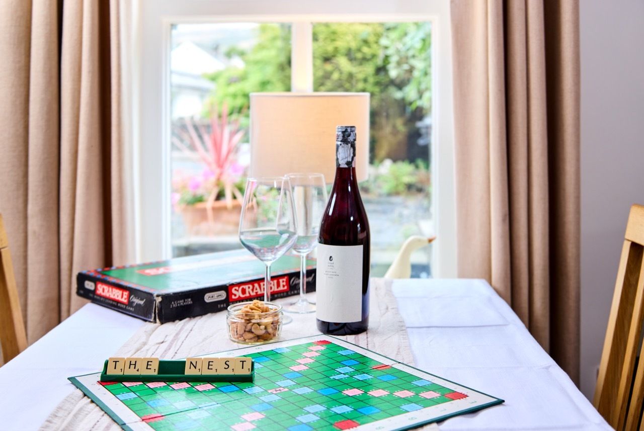 A Scrabble board game, a bottle of wine, two glasses, and a window with curtains.