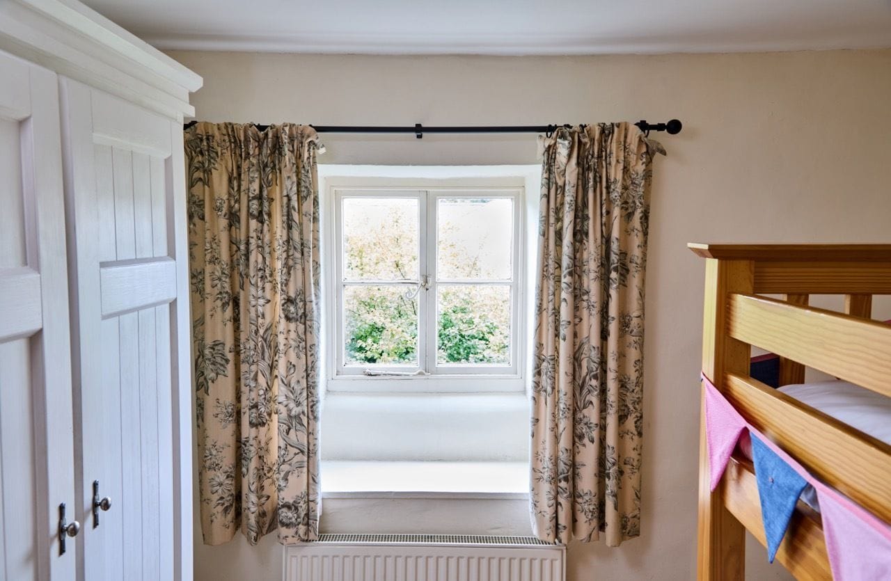 Ein Zimmer mit Fenster, Heizkörper, einem hölzernen Bett und Vorhängen.
