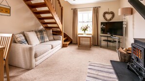 Un salon chaleureux avec un escalier en bois, un canapé, une télévision, une cheminée et une fenêtre avec des rideaux.