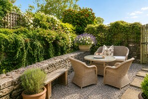 Een terras met rieten meubels, een stenen muur en verschillende planten.