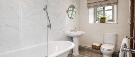 A bathroom with a freestanding bathtub, a pedestal sink, a toilet, and a window with a view of greenery.