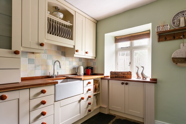 A kitchen with white cabinets, a wooden countertop, a window with blinds, and a view of the outside.