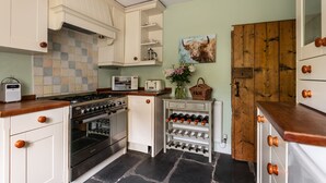 Une cuisine avec des meubles blancs, une cuisinière, un four, un meuble à vin et une porte en bois.