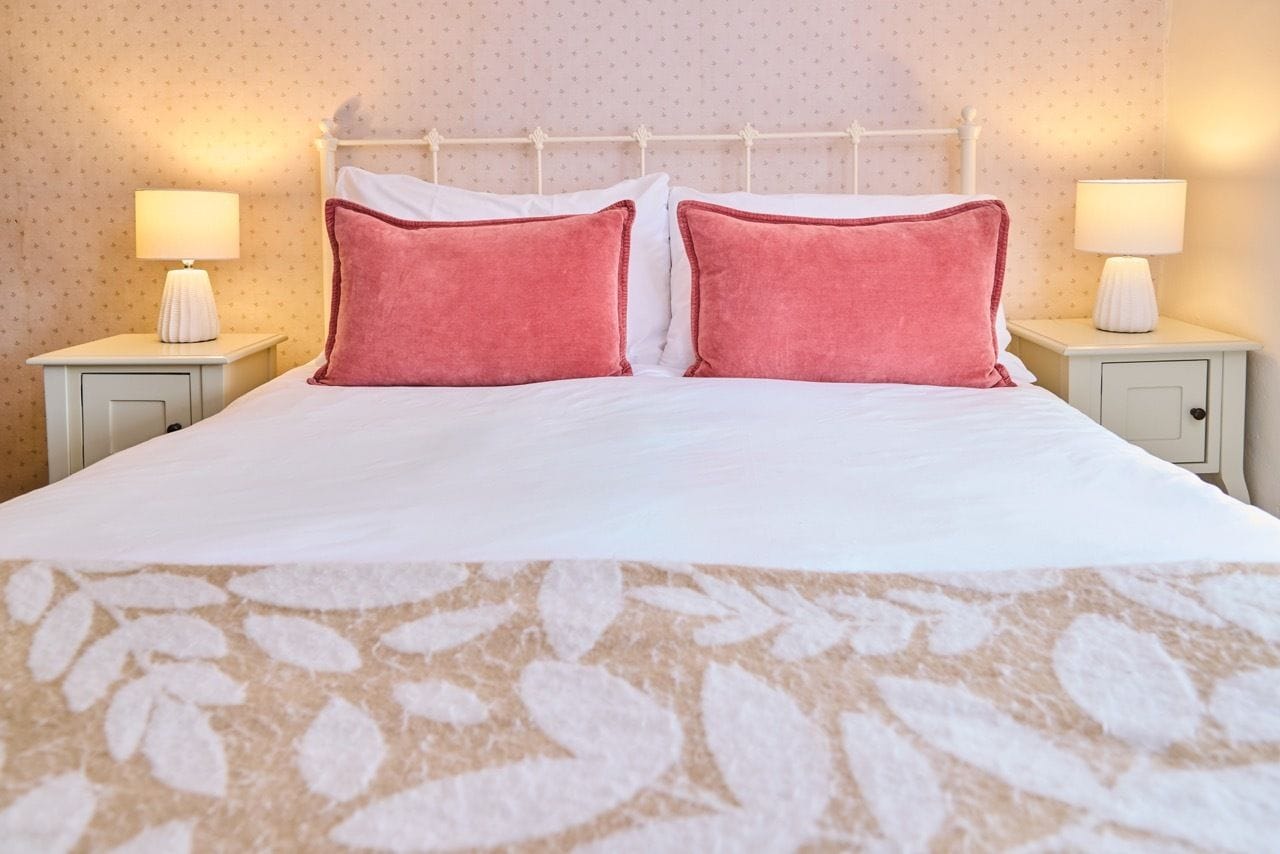 A neatly made bed with a white and pink color scheme, flanked by two bedside tables with lamps.