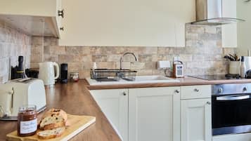 Una cocina moderna con armarios blancos, encimera de madera, horno integrado y salpicadero de piedra.