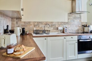 A modern kitchen with white cabinets, a wooden countertop, a built-in oven, and a stone backsplash.
