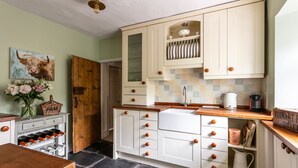 Una cocina con armarios blancos, encimera de madera y salpicadero de azulejos. Hay un fregadero, una cafetera y una vinoteca.