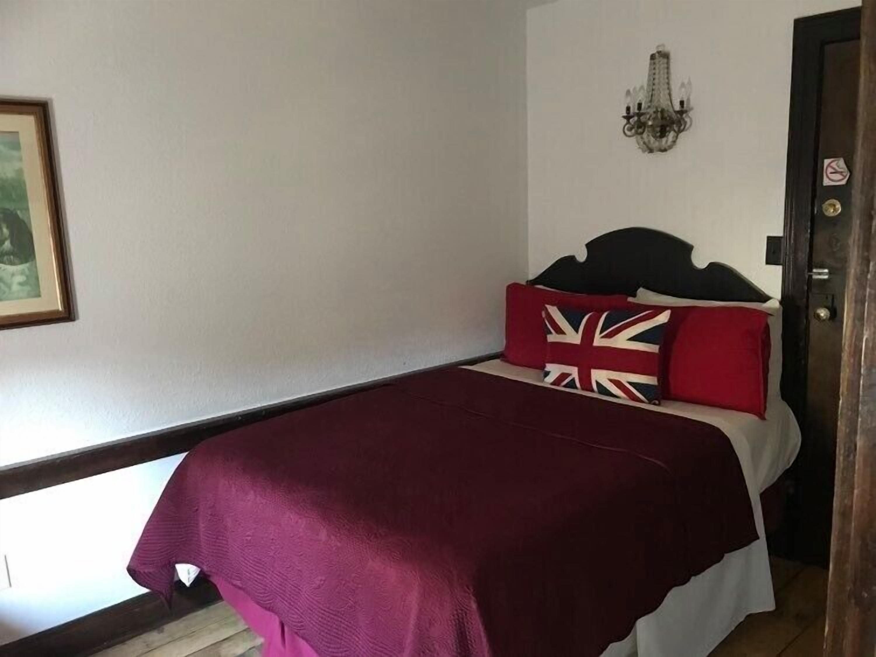 A bed with a dark headboard, a red pillow, and a Union Jack pillow.