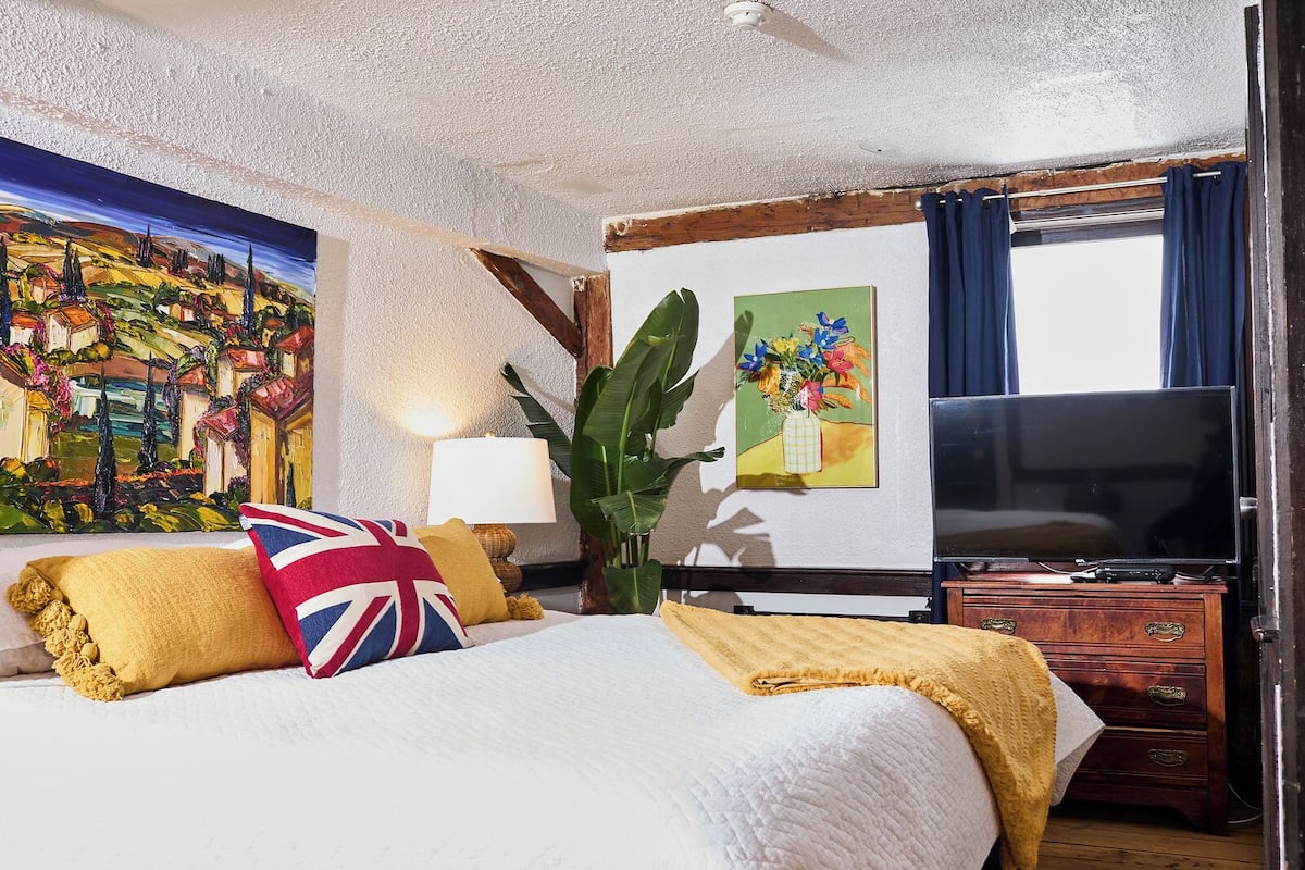 A hotel room with a large bed, a flat-screen TV, a wooden dresser, and a painting on the wall.