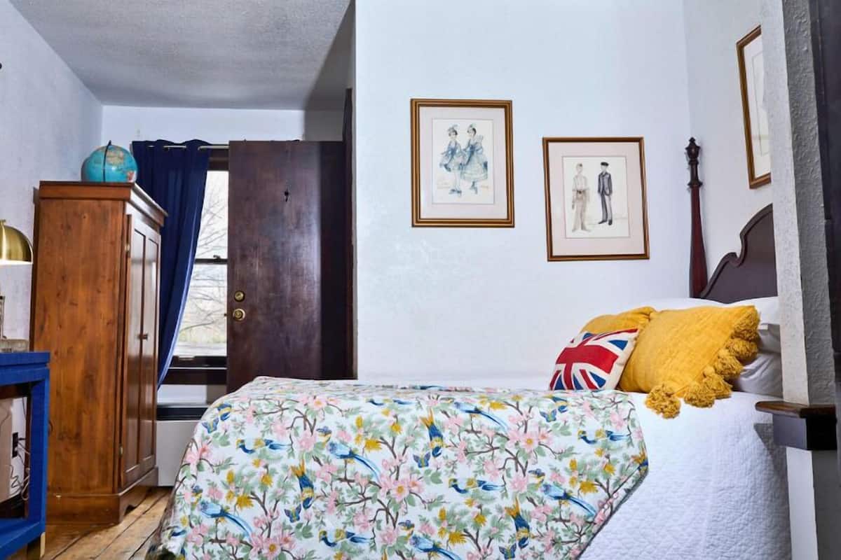 A bedroom with a floral bedspread, a wooden wardrobe, a globe on a cabinet, and two framed pictures on the wall.