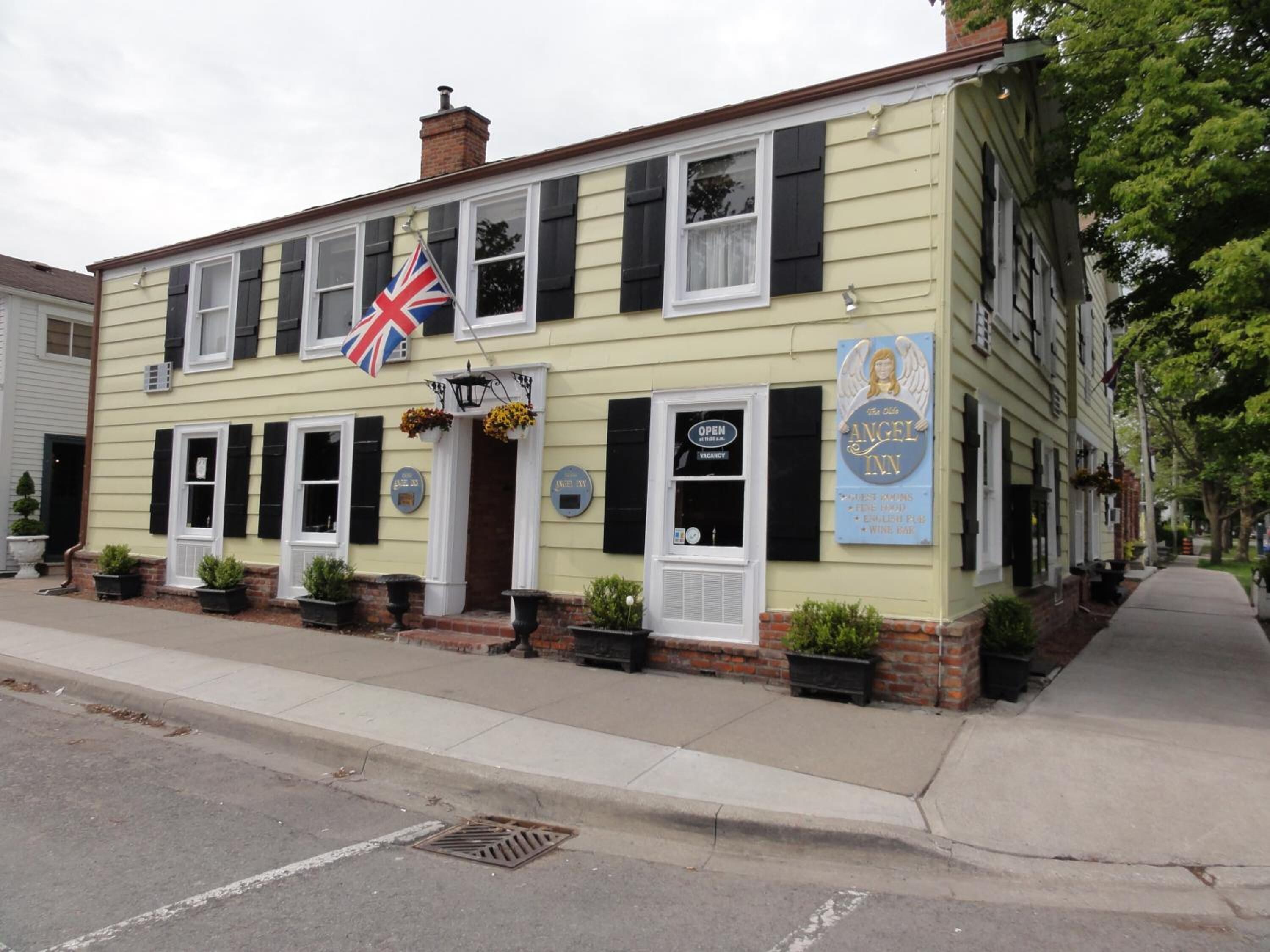 Un bâtiment à deux étages, orné d’un drapeau britannique, d’une enseigne indiquant « The Angel Inn » et énumérant les services proposés, et doté d’une façade en briques.